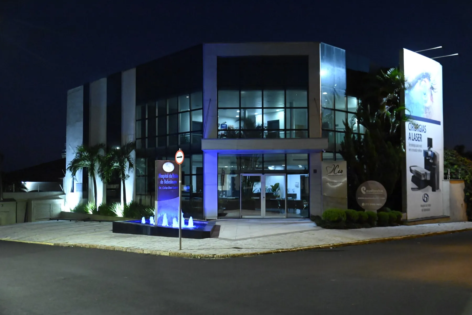 Fachada iluminada do Hospital da Visão de Bebedouro à noite, com fonte de água na entrada